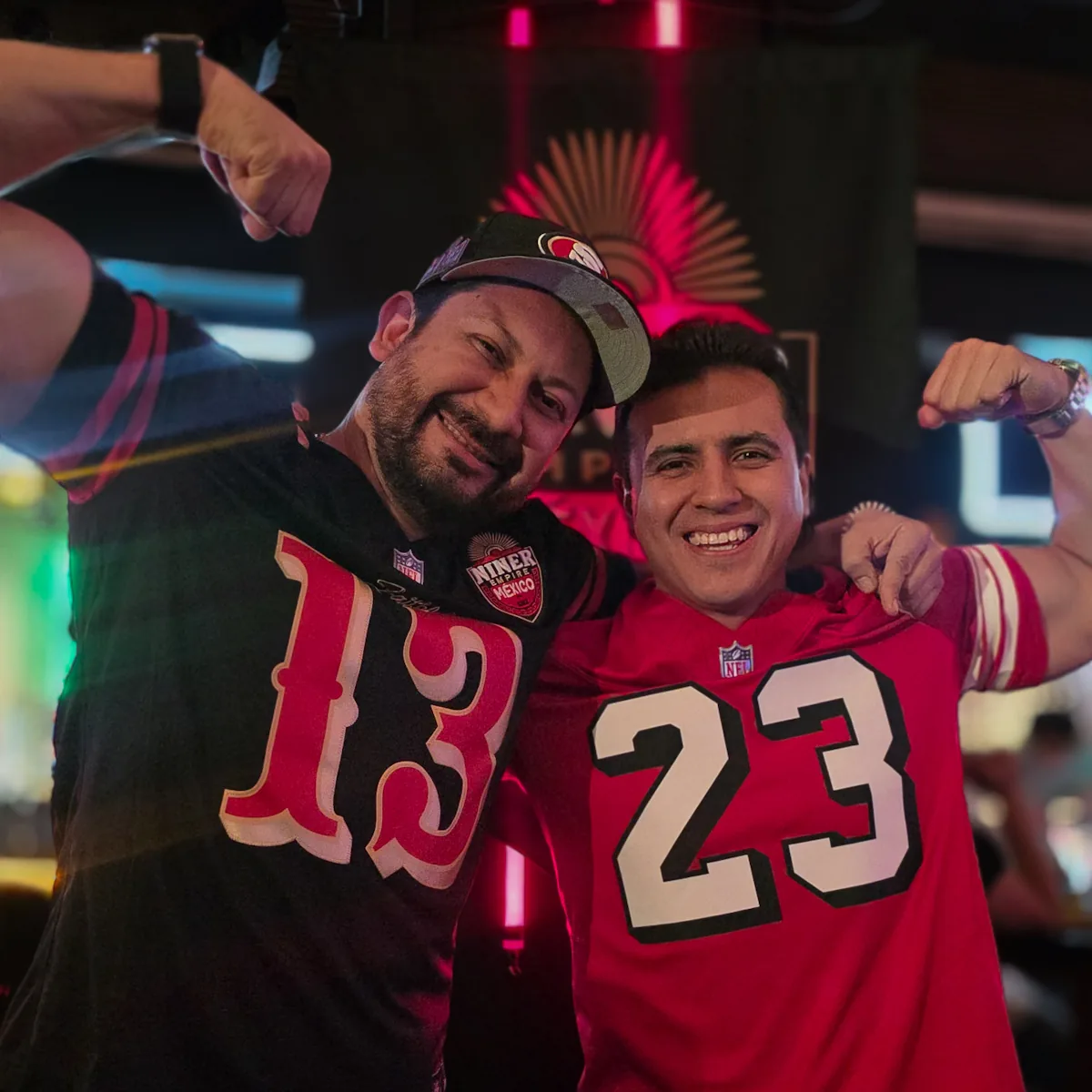 Dos miembros con jerseys 13 y 23 de los 49ers marcando bíceps en el watch party