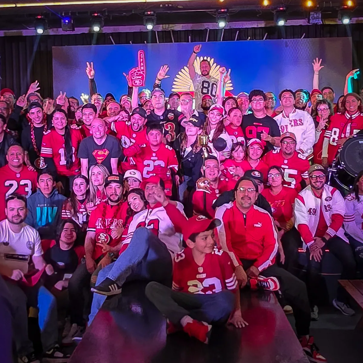 Decenas de miembros de Niner Empire México posando juntos en el escenario del watch party