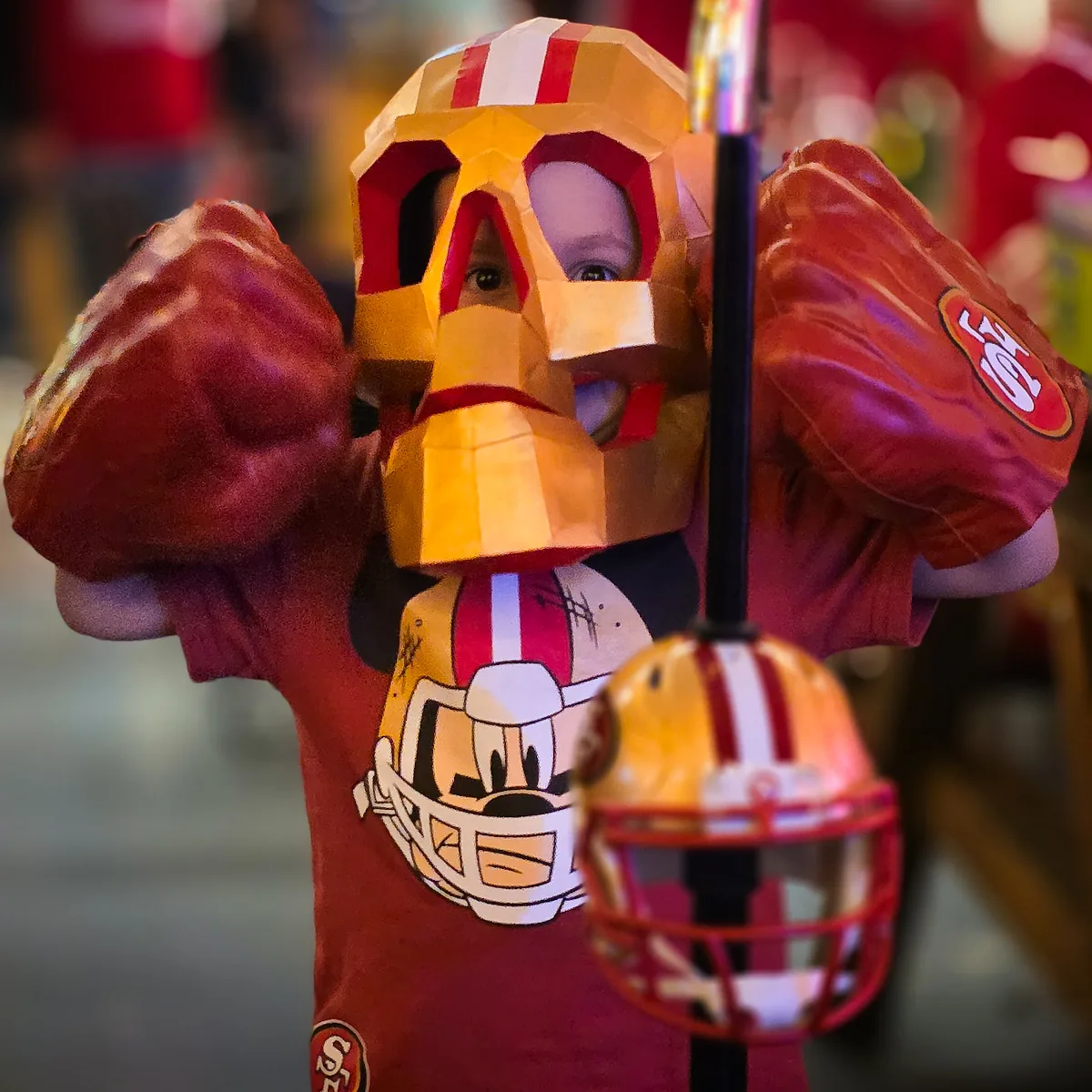 Miembro con máscara de calavera de papel en rojo y dorado, guantes de hule y casco de los 49ers