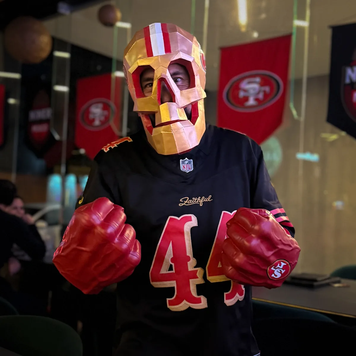 Miembro con máscara de calavera de papel, jersey 44 y puños de hule rojos frente a los banderines