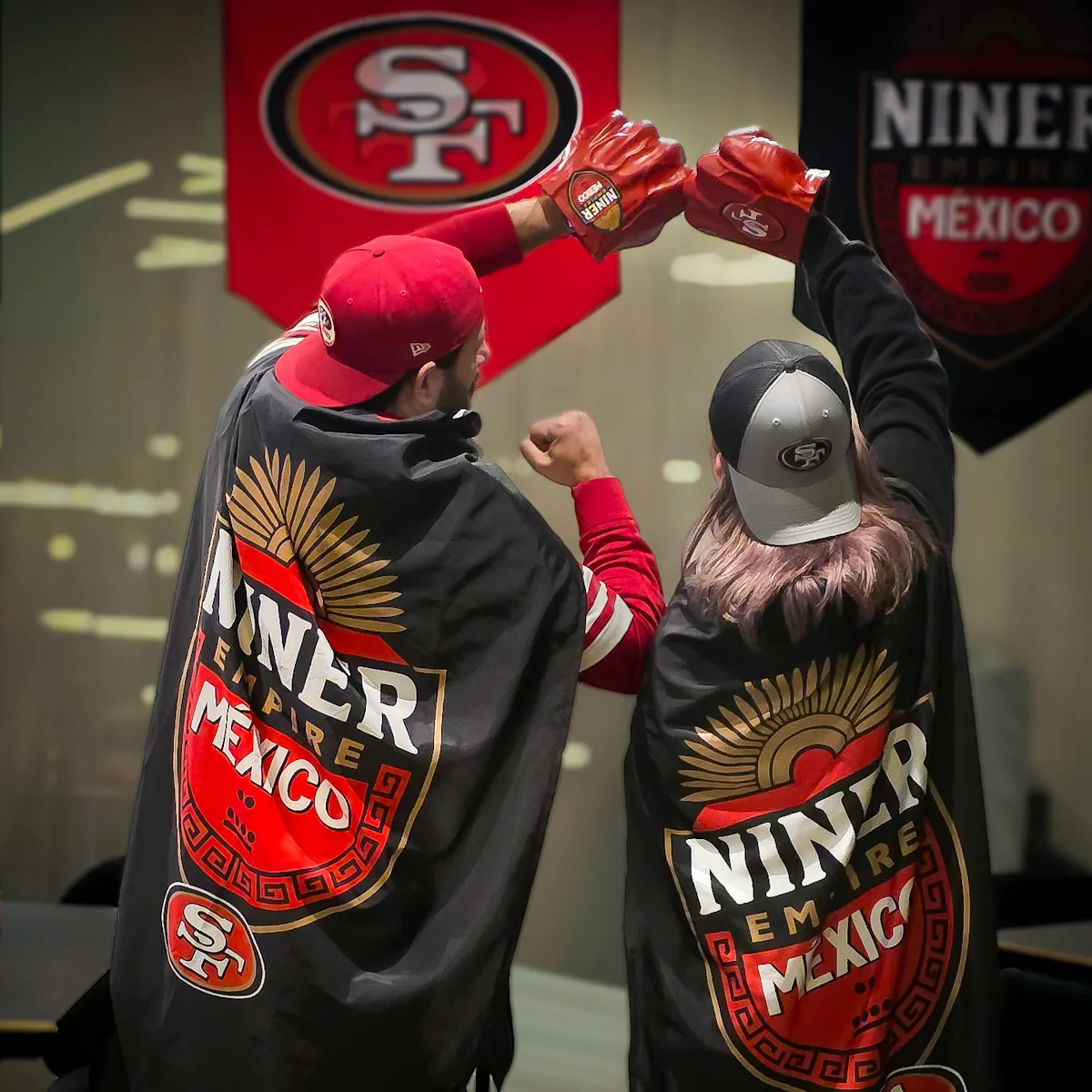 Dos miembros de espaldas con las capas de Niner Empire México chocando los guantes