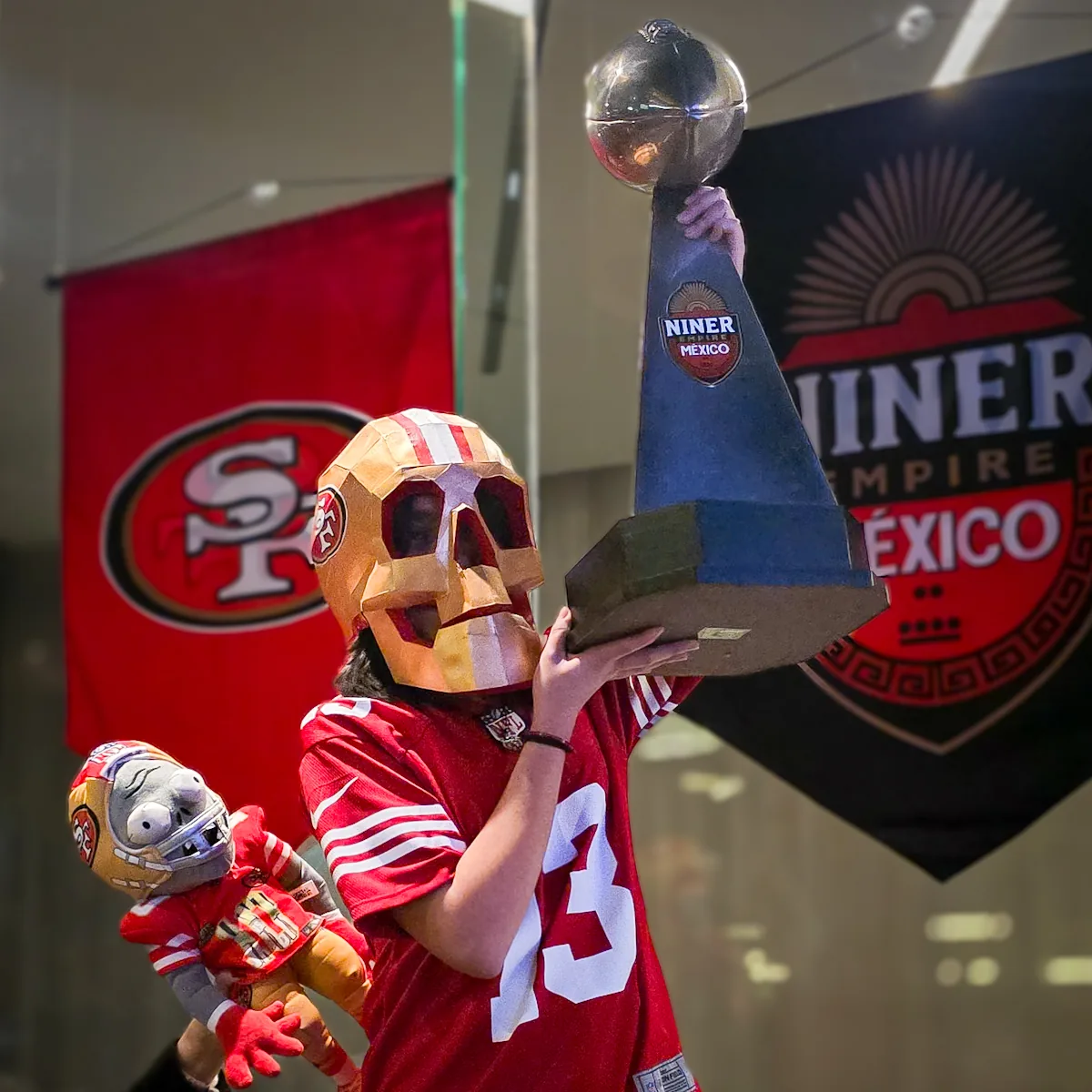 Miembro con máscara de calavera levantando un trofeo junto a los estandartes de Niner Empire México