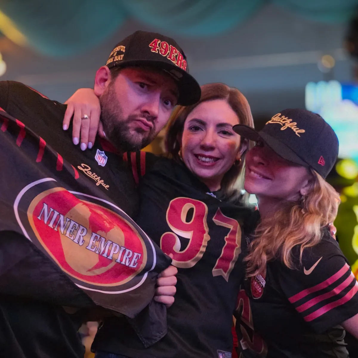 Tres miembros abrazados con jerseys y playeras de Niner Empire y los 49ers